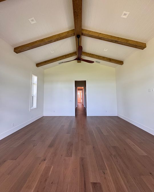 A bedroom with wood ceiling beams and a hardwood floor running to the hallway.