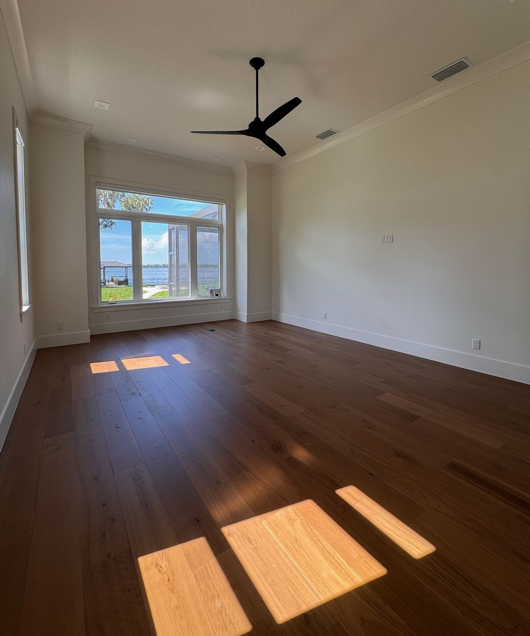The same bedroom when done, with a wide-plank hardwood floor and sunlight across it.