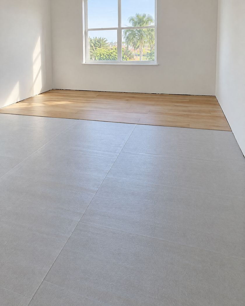 Empty room with the slab under smooth gray underlayment, the first rows of a new oak floor along the far wall and bare walls with no baseboards yet.